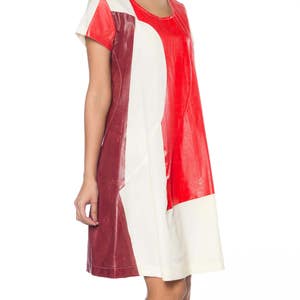 Puede incluir: Un vestido con bloques de color con un dise&ntilde;o audaz. El vestido combina paneles rojos, crema y burdeos. Tiene mangas cortas y un escote redondo. El vestido llega a la rodilla y parece estar hecho de un material similar al cuero.