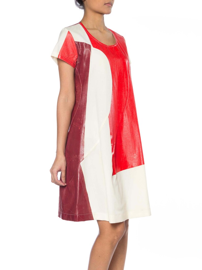 Puede incluir: Un vestido con bloques de color con un dise&ntilde;o audaz. El vestido combina paneles rojos, crema y burdeos. Tiene mangas cortas y un escote redondo. El vestido llega a la rodilla y parece estar hecho de un material similar al cuero.