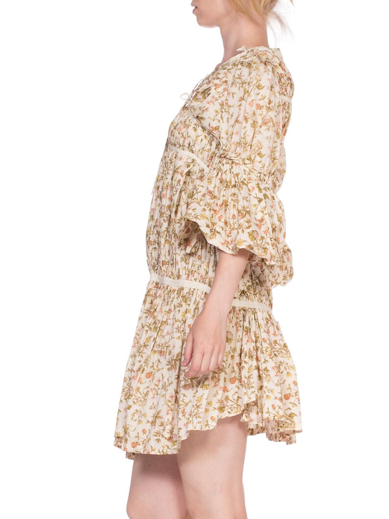 May include: A white floral print mini dress with a gathered skirt and 3/4 sleeves. The dress has a V-neckline and a tie at the neckline.