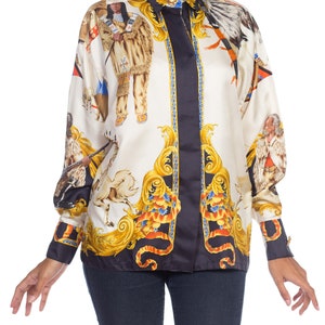 May include: A white silk button-down shirt with a black and gold print featuring Native American figures, horses, and ornate designs.