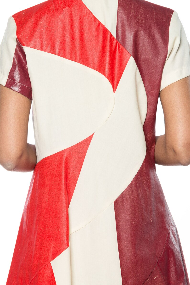 Puede incluir: Vestido de manga corta con dise&ntilde;o geom&eacute;trico en rojo, crema y burdeos. El vestido presenta un patr&oacute;n &uacute;nico con formas angulares y una silueta entallada. La tela parece tener un acabado texturizado similar al cuero.