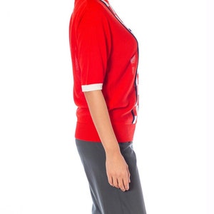 May include: A red short-sleeved sweater with white and blue geometric patterns. The sweater is made of a soft, knit fabric.