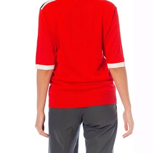 May include: A red short-sleeved sweater with white and black trim on the shoulders and sleeves.