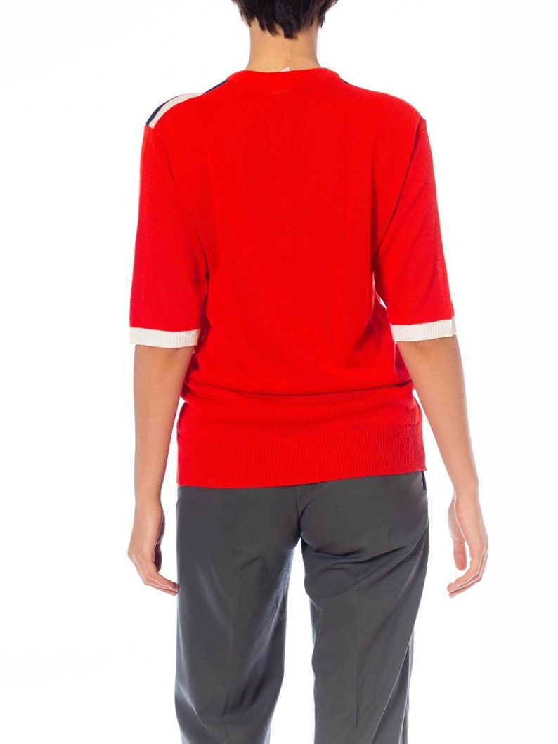 May include: A red short-sleeved sweater with white and black trim on the shoulders and sleeves.