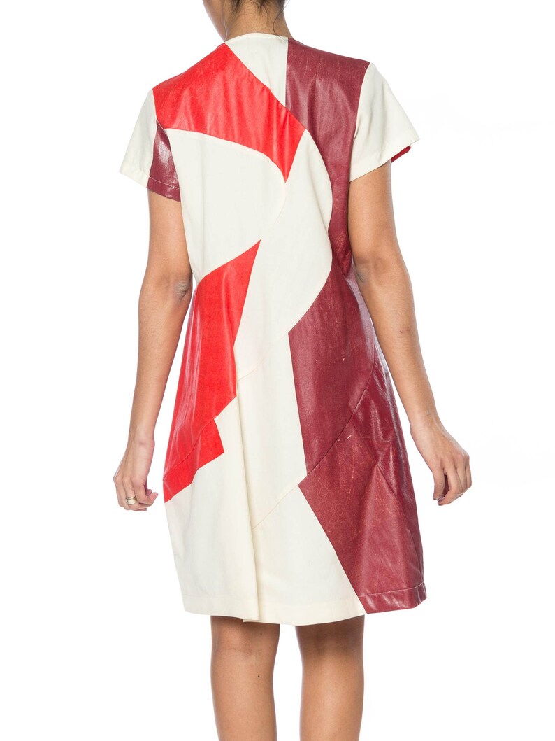 Puede incluir: Vestido de manga corta con dise&ntilde;o geom&eacute;trico. El vestido presenta un patchwork de paneles rojos, crema y burdeos. El vestido tiene un corte sencillo y recto y parece estar hecho de un material texturizado.