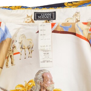 May include: A white silk shirt with a colorful print of horses, riders, and a gold design. The shirt has a label that reads "Gianni Versace" and a size tag that says "38".