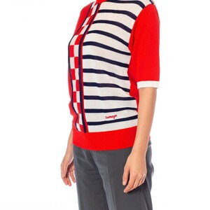 May include: A red, white, and blue striped knit sweater with a checkered pattern on the side. The sweater has short sleeves and a crew neck. The brand name "Cosmopolitan" is embroidered on the front.