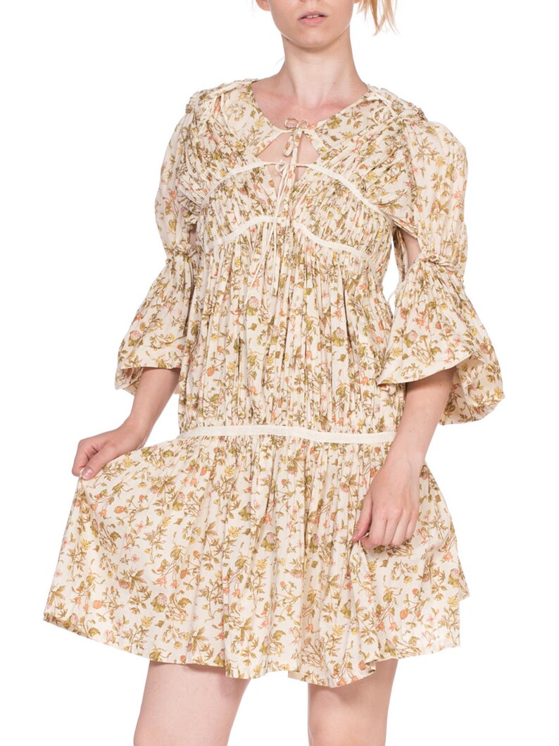 May include: A white floral print dress with a tie at the neckline and 3/4 sleeves. The dress has a gathered skirt and a relaxed fit.