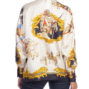 May include: A white silk blouse with a long sleeve and a button-up collar. The blouse features a colorful print of a man with a rifle, horses, and other figures. The print is in a baroque style with gold accents.