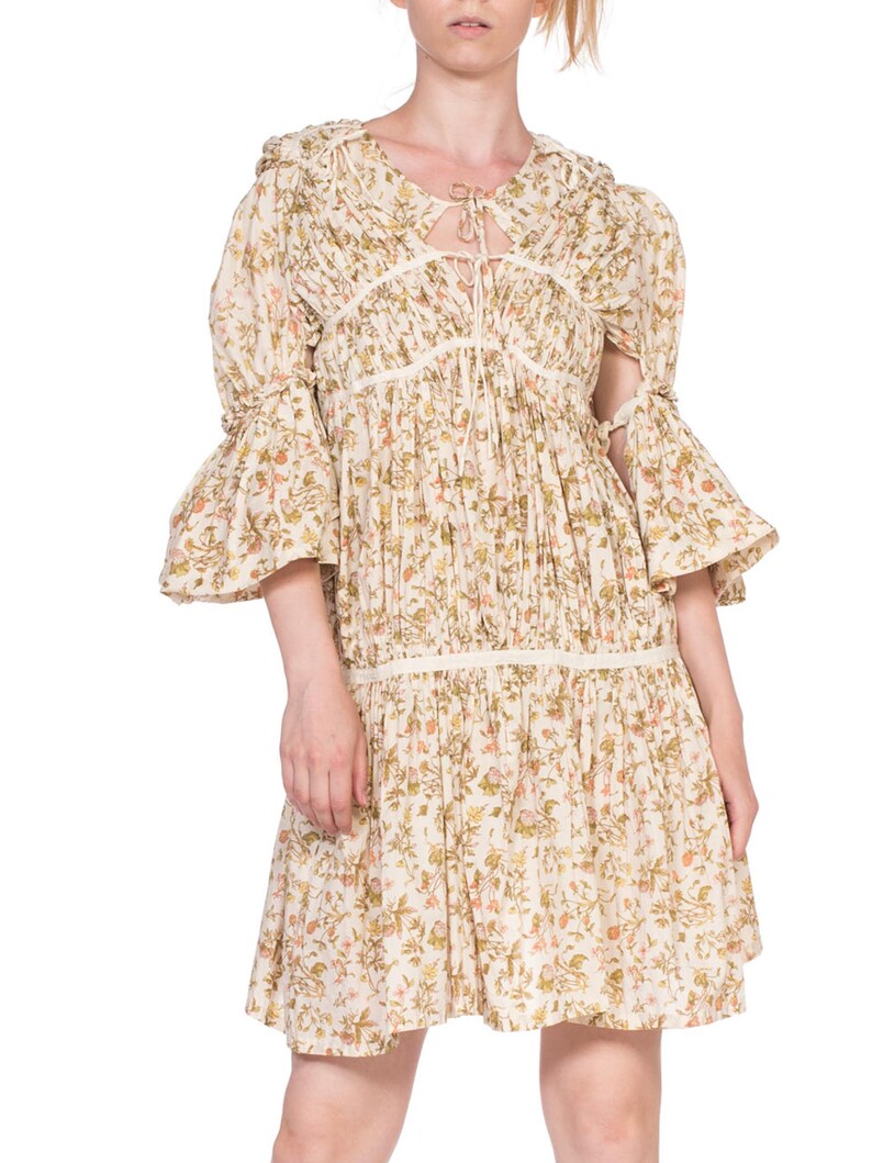 May include: A white floral print dress with a tie at the neckline and bell sleeves. The dress has a gathered skirt and a lace trim.