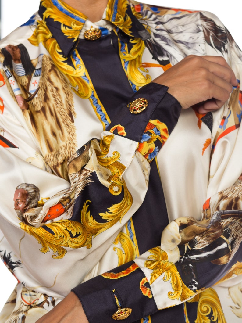 May include: A white and black silk shirt with a gold and brown print of a horse and rider. The shirt has a button-up collar and long sleeves with gold buttons.