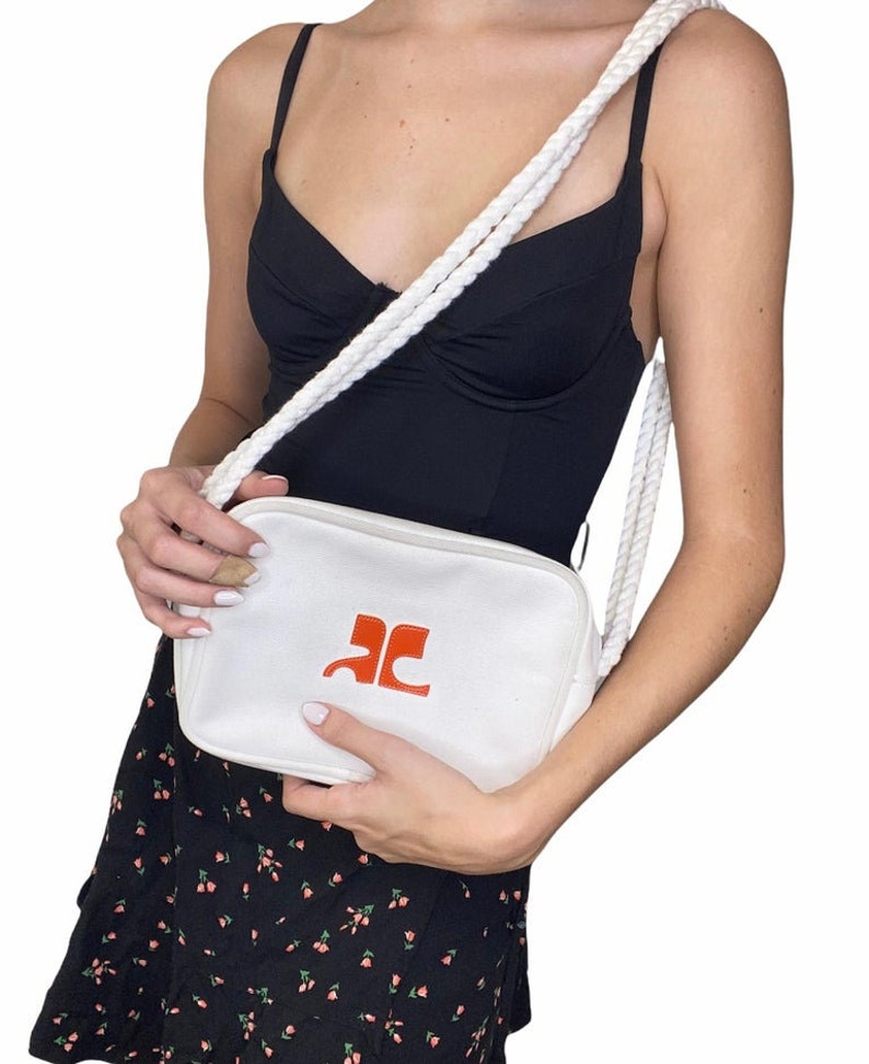 May include: White canvas crossbody bag with a rope strap and a red logo that says "AC".