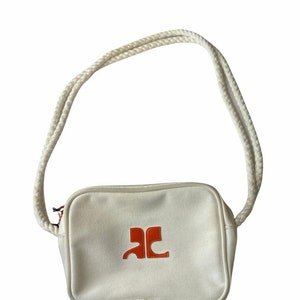 May include: A white canvas crossbody bag with a rope strap and an orange logo that says "AC".