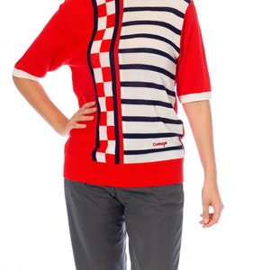 May include: Red, white, and blue striped and checkered short-sleeved sweater with the word "Cotswold" on the bottom right side.
