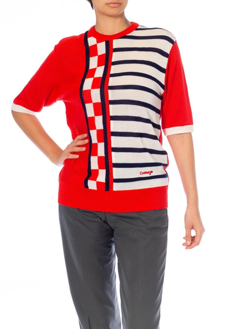 May include: Red, white, and blue striped and checkered short-sleeved sweater with the word "Cotswold" on the bottom right side.