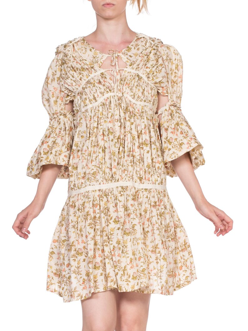 May include: A white floral print dress with a tie at the neckline and bell sleeves. The dress has a gathered skirt and a relaxed fit.