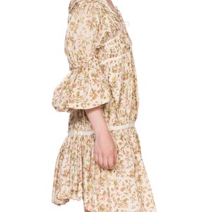 May include: A white cotton dress with a floral print and a gathered skirt. The dress has a V-neckline and 3/4 sleeves with ruffles at the cuffs.