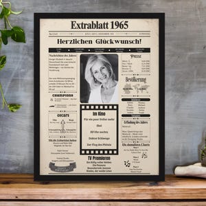 Könnte beinhalten: Ein gerahmtes, im Vintage-Stil gestaltetes Zeitungsplakat mit dem Titel Extrablatt 1965 und schwarzem Rahmen. Der Druck zeigt ein zentrales Schwarz-Weiß-Porträt, historische Schlagzeilen, Filmtitel und Tabellen in deutscher Sprache auf beigem Grund.