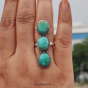 May include: A silver ring featuring three vertically aligned oval turquoise stones. Each stone is set in a twisted rope-style silver bezel. The ring band is plain silver, and the stones display natural blue-green color variations with dark matrix.