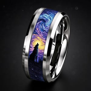 Op de afbeelding: Een gepolijste zilverkleurige metalen ring met een brede inleg met een levendig, wervelend nachthemelpatroon in blauwe, paarse en gele tinten. Het ontwerp toont het silhouet van een wolf die naar een heldere, gloeiende ronde maan huilt.