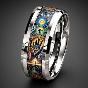 May include: A polished silver-tone metal ring featuring a wide, flat band with a colorful, intricate inlay. The inlay displays a detailed cosmic scene with a central hand, an eye, a pyramid, celestial bodies, and figures in vibrant shades of blue, orange, and gold.