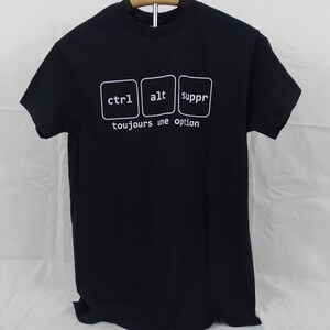 May include: A black short-sleeved t-shirt featuring a white graphic of three rounded square keys labelled ctrl, alt, and suppr. Below the keys, the white text reads toujours une option. The shirt has a crew neckline and is displayed on a hanger.