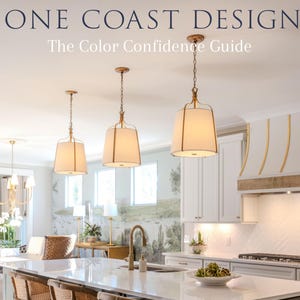 May include: A kitchen interior featuring three gold-toned pendant lights with white fabric shades hanging over a large white quartz island. Three wooden bar stools with woven cane backs are positioned at the island, which has a gold faucet.