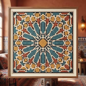 May include: A square cross-stitch embroidery featuring a geometric star pattern in shades of teal, mustard yellow, and terracotta, outlined in black thread on a cream fabric background, encased in a simple light brown wooden frame.