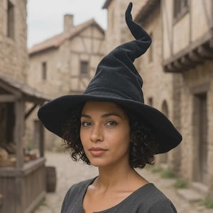 Peut inclure: Un chapeau pointu noir doté d'un large bord circulaire et d'une calotte haute légèrement incurvée. Le chapeau est fabriqué dans un tissu sombre et uni à la texture lisse, avec un sommet distinct qui s'effile en pointe au sommet de la calotte.