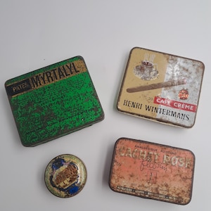 Peut inclure: Quatre boîtes en métal vintage de formes et tailles variées. L'une est verte avec le texte PATES MYRTALYL, une carrée avec un cigare et une tasse de café marquée HENRI WINTERMANS, une petite boîte ronde et une rectangulaire marquée CACHET ROSK.