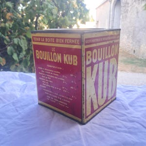 Peut inclure: Une boîte métallique carrée pour Bouillon Kub avec des panneaux rouges et jaunes et du texte noir. La face avant affiche le nom de la marque en grandes lettres, tandis que le côté liste la composition et les instructions, dont Tenir la boite bien fermee.