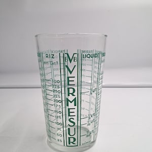 Puede incluir: Una taza medidora de vidrio transparente con marcas y texto impresos en verde. El texto vertical dice VERMESUR, con etiquetas adicionales para RIZ en Grs y LIQUIDE. La taza incluye escalas de medición graduadas para varios ingredientes en gramos y litros.