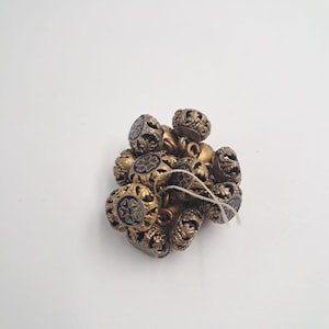Peut inclure: Un ensemble de petits boutons métalliques ronds présentant un design complexe en filigrane ajouré. Plusieurs boutons sont ornés d'une incrustation circulaire en émail bleu affichant un motif floral central dans des tons rouge et or.