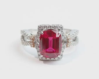 May include: A silver ring featuring a large, rectangular, cushion-cut vibrant red gemstone at the center. The stone is surrounded by a halo of small, clear, round-cut diamonds, with additional diamonds set along the split-shank band.