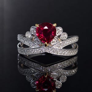 Puede incluir: Un anillo de tono plateado con una gran piedra preciosa roja en forma de pera en el centro. La banda y el engaste están incrustados con numerosas piedras pequeñas y claras en pavé. El diseño incluye una disposición en forma de corona central.