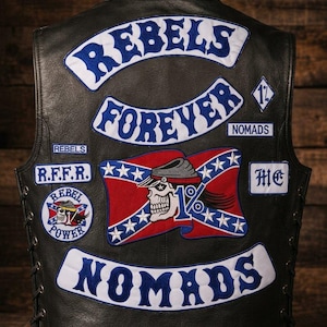 May include: A black leather waistcoat featuring multiple embroidered patches. The back displays the text REBELS FOREVER and NOMADS in blue and white. A central patch shows a skull wearing a cap over a red, white, and blue flag with 1% text.