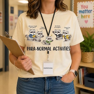 Puede incluir: Una camiseta de color crema con un gráfico de cinco mapaches de dibujos animados con globos de texto que dicen: did you track the data?, i have goldfish!, we have an eloper!, y Check the BIP!. Debajo de los mapaches, el texto PARA-NORMAL ACTIVITIES.