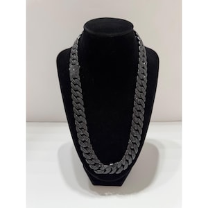 May include: A black cuban link chain necklace featuring a continuous pattern of interlocking, pavé-set black stones throughout the entire length of the metal links, including a rectangular box clasp closure that is also encrusted with black stones.