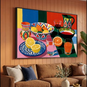 Puede incluir: Una impresión de arte mural rectangular que presenta un bodegón vibrante de cítricos, cuencos de cerámica estampados, una jarra y cristalería. La composición incluye limones amarillos, rodajas de naranja y diseños geométricos coloridos sobre un fondo audaz y multicolor de paneles azules, verdes, rojos y rosas.