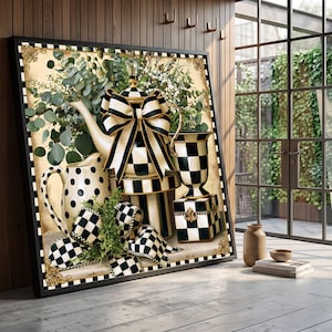 May include: A framed wall art print featuring a teapot, a pitcher, and a vase decorated with black and white checkered and polka dot patterns. The teapot is adorned with a large black and white striped bow, surrounded by green eucalyptus foliage.