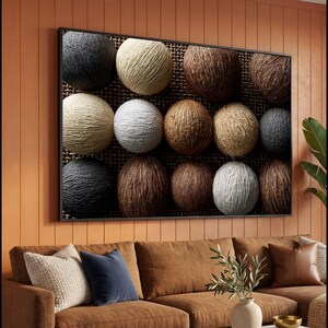 May include: A rectangular framed wall art piece featuring a grid of twelve spherical objects with varied textures and colours, including shades of black, white, beige, and brown, set against a dark, coarse, woven fabric background.
