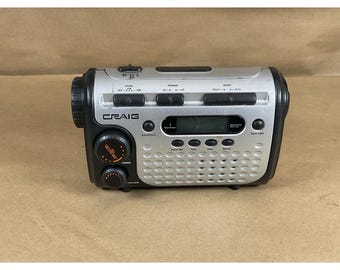 Può includere: Una radio portatile Craig argento e nera con display a orologio digitale, interruttori di alimentazione e banda sulla parte superiore e manopole frontali per volume e sintonizzazione. Dotata di griglia altoparlante forata.