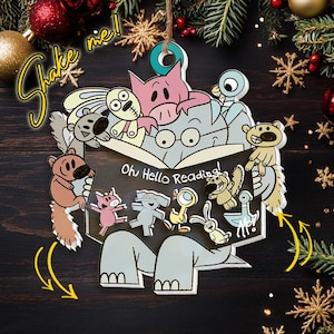 May include: A decorative hanging ornament featuring a gray elephant reading a book with the text Oh Hello Reading! surrounded by various cartoon animals including a pig, rabbit, and bird. The ornament includes the text Shake me!