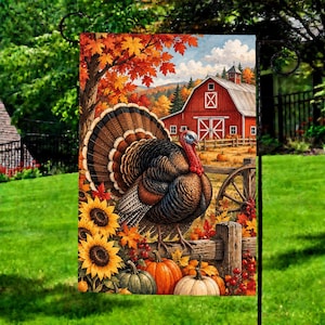May include: A decorative garden flag featuring a turkey with fanned tail feathers standing on a wooden fence. The scene includes bright yellow sunflowers, orange pumpkins, and a red barn in the background under a blue sky with autumn foliage.