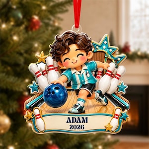 May include: A Christmas tree ornament featuring a cartoon character bowling with a blue ball on a wooden lane. The character wears a teal shirt and black shorts. White bowling pins surround the scene. A banner displays the text ADAM 2026.