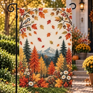 May include: A rectangular garden flag featuring a fall scene with a black-capped chickadee perched on a branch, falling autumn leaves, pine trees, distant snow-capped mountains, and white daisies with red berries on a cream-colored background.
