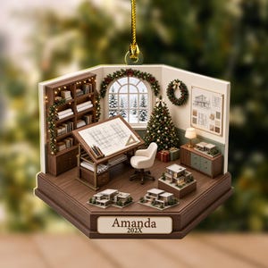 May include: A hexagonal hanging ornament featuring a miniature architectural office scene with a drafting table, bookshelf, and Christmas tree. The base displays the name Amanda and the year 202X. The room includes a window view of snowy trees.