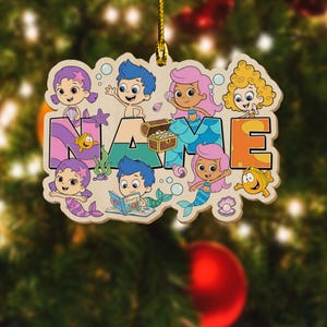 May include: A wooden ornament featuring Bubble Guppies characters including Gil, Molly, Deema, and Oona, with a treasure chest, sea creatures, and the word NAME in large colorful letters. It includes a gold string for hanging on a tree.