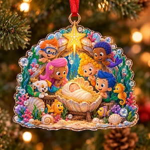 May include: A decorative acrylic ornament featuring a nativity scene with Bubble Guppies characters surrounding a baby in a seashell cradle. The design includes a yellow starfish, colorful coral, seashells, and bubbles, all suspended by a red ribbon.