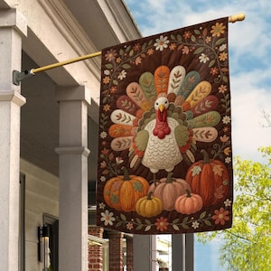 May include: A rectangular garden flag featuring a central turkey with a colorful, patterned tail fan. Below the turkey are four pumpkins in shades of orange, tan, and pink. The dark brown background is decorated with a border of white and orange flowers.
